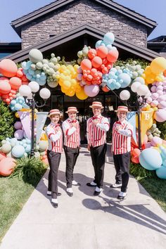 three men in red and white striped shirts standing under an arch with balloons