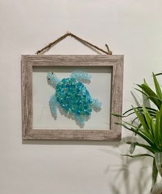 a sea turtle made out of glass is hanging on the wall next to a potted plant