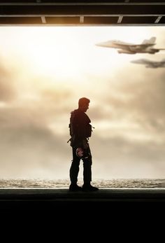 a man standing in front of an airplane looking out at the ocean with his back to the camera