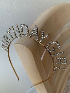 a tiara made out of wood with crystal letters on the top and bottom, sitting on a wooden stand