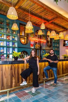 two people sitting at a bar in front of some hanging lights and lamps above them