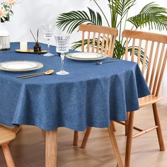 a blue table cloth with white plates and silverware on it, next to two wooden chairs