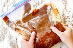 a person holding a bag filled with food on top of a wooden table next to a knife