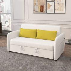 a white couch with two yellow pillows on it in front of a window and table