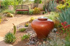 a large vase sitting in the middle of a garden with rocks and plants around it