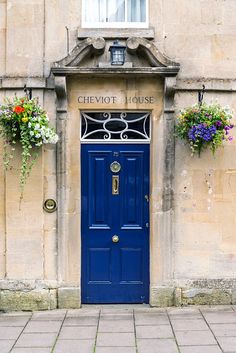 a blue door with flowers hanging from it's sides on the side of a building