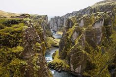 a river flowing between two large rocks in the middle of a valley with moss growing on it