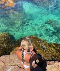 a woman sitting on top of a rock next to the ocean with clear blue water