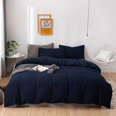 a bed with blue sheets and pillows in a white room next to a cat on the floor