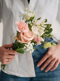 a close up of a person holding a bouquet of flowers in their hands and wearing a white shirt