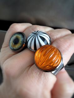 "Retro and so much fun -- bright, neon orange pumpkin ring for Halloween! This fluorescent orange ribbed acrylic vintage cabochon has incredible visual depth -- it reflects light as if it were glowing! The vintage cabochon is set in a black bezel on a flexible metal, decorative gothic filigree adjustable ring band. The ring fits most adults (size 5 to 9), but it may be loose on smaller fingers. - Vintage acrylic orange cabochon: 3/4\" (18mm) dia, 1/2\" (12mm) tall - Flexible black filigree ring: Ring Trick, Gothic Filigree, Black Band Ring, Pumpkin Ring, Halloween Ring, Hardware Jewelry, Fluorescent Orange, Cosplay Jewelry, Halloween Eyeballs