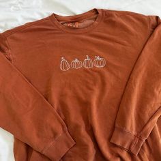 an orange sweatshirt with three pumpkins embroidered on the front and two smaller ones at the back