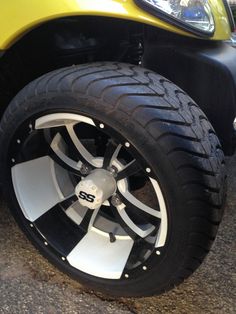 the front wheel of a yellow car with black and white spokes on it's tires