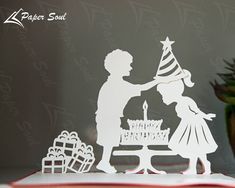 a paper cut out of a man and woman at a table with a birthday cake