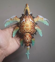 a hand holding a paper model of a turtle with wings and claws on it's head