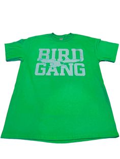 Bird Gang Green T-Shirt (New) Philly Edition. Green T-Shirt with Metallic Silver Print on chest.  6 oz/yd2 | 10 oz/ly | 203 g/m2 100% cotton  Set-in rib collar with shoulder-to-shoulder taping Double-needle sleeve and bottom hem Preshrunk to minimize shrinkage Green Tops With Graphic Design For Fan Merchandise, Green Fan Apparel T-shirt With Screen Print, Green Pre-shrunk Band Merch T-shirt, Green Fan Merchandise T-shirt With Text Print, Green T-shirt With Text Print For Fans, Green Text Print T-shirt For Fans, Green Fan Apparel T-shirt With Logo Print, Green Fan Apparel T-shirt With Logo, Green Tops With Logo Print For Fan Merchandise