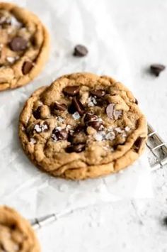 three chocolate chip cookies sitting on top of a white table next to some spoons