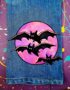 two bats are flying in front of a full moon painted on blue denim fabric with splats