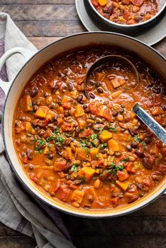 two bowls filled with chili and beans on top of a wooden table next to a spoon