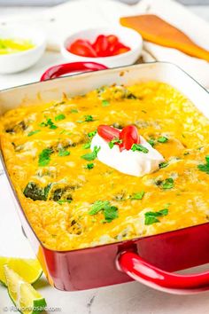 a red casserole dish filled with broccoli, cheese and sour cream