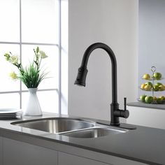 a kitchen sink sitting under a window next to a vase filled with flowers and fruit