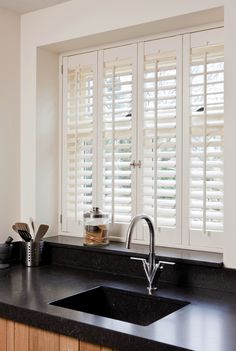 a kitchen sink sitting next to a window covered in shutters