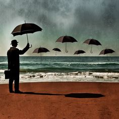 a man standing on top of a sandy beach holding an umbrella over his head and looking at the ocean