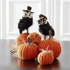 three knitted pumpkins sitting on top of each other with two black birds perched on them