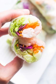 a hand holding a small sandwich with shrimp, lettuce and carrots