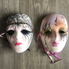 two masquerade masks are sitting on the floor, one is white and the other is pink