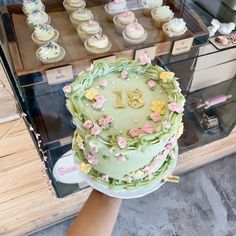 a person holding a cake with flowers on it in front of some cupcakes