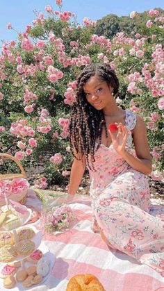 a woman sitting on a pink and white checkered blanket with food in front of her