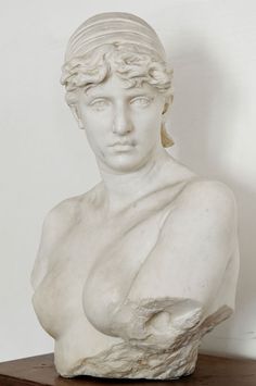 a marble bust of a woman with her arms crossed and eyes closed, sitting on a wooden table