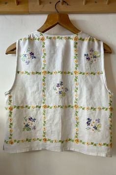 a white top with flowers on it hanging from a wooden hanger next to a wall