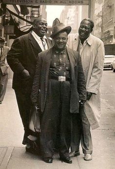 an old photo of three men standing next to each other on the sidewalk in front of a building