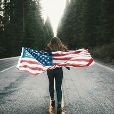 a woman walking down the road holding an american flag