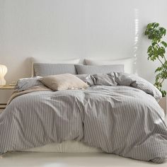 a bed with grey and white striped comforter next to a potted green plant