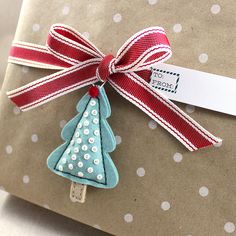 a gift wrapped in brown paper with a red ribbon and a christmas tree ornament