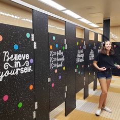 a woman is standing in front of some black stalls with colorful writing on the walls