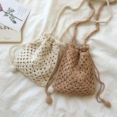 two small crocheted bags sitting on top of a bed next to a book