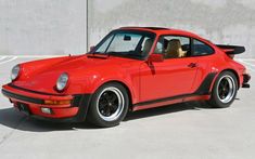 a red porsche parked in a parking lot next to a concrete wall with the door open