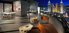 a balcony with tables, chairs and couches overlooking the city skyline at night time