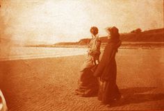 two women standing on the beach looking out at the water