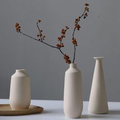 three white vases sitting on top of a table next to each other with flowers in them