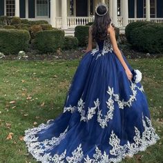 a woman in a blue ball gown standing on the grass with her back to the camera