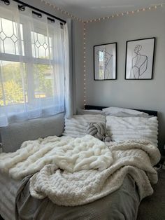 an unmade bed with white blankets and lights on the window sill above it