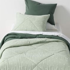 a bed with green comforter and pillows on it's headboard, next to a white wall