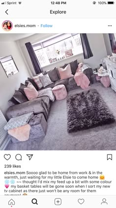 a living room with grey couches and pink pillows on the floor in front of a window