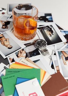 an assortment of polaroid photos and a watch on a table with a glass of alcohol