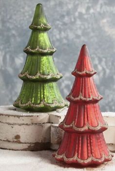 two red and green ceramic christmas trees sitting on top of white brick wall next to each other